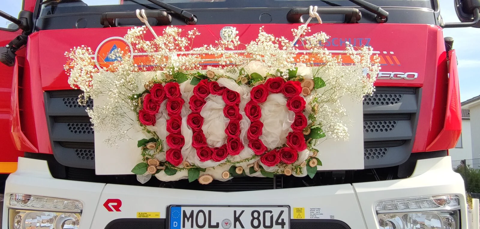 Blumenschmuck am Kühlergrill des Löschfahrzeugs: die Zahl 100 aus roten Rosen, umrahmt von Schleierkraut