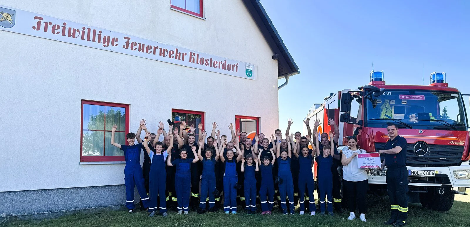 Die Freiwillige Feuerwehr Klosterdorf und die Jugendfeuerwehr jubeln vor dem Gerätehaus nach der Scheckübergabe der Sparkasse